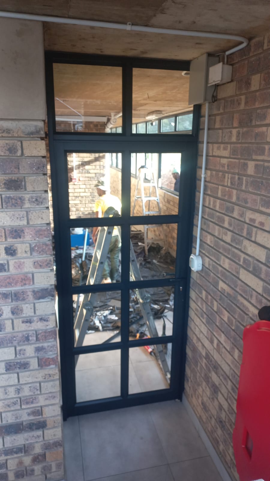 Dark-framed aluminium glass door installed in a brick corridor